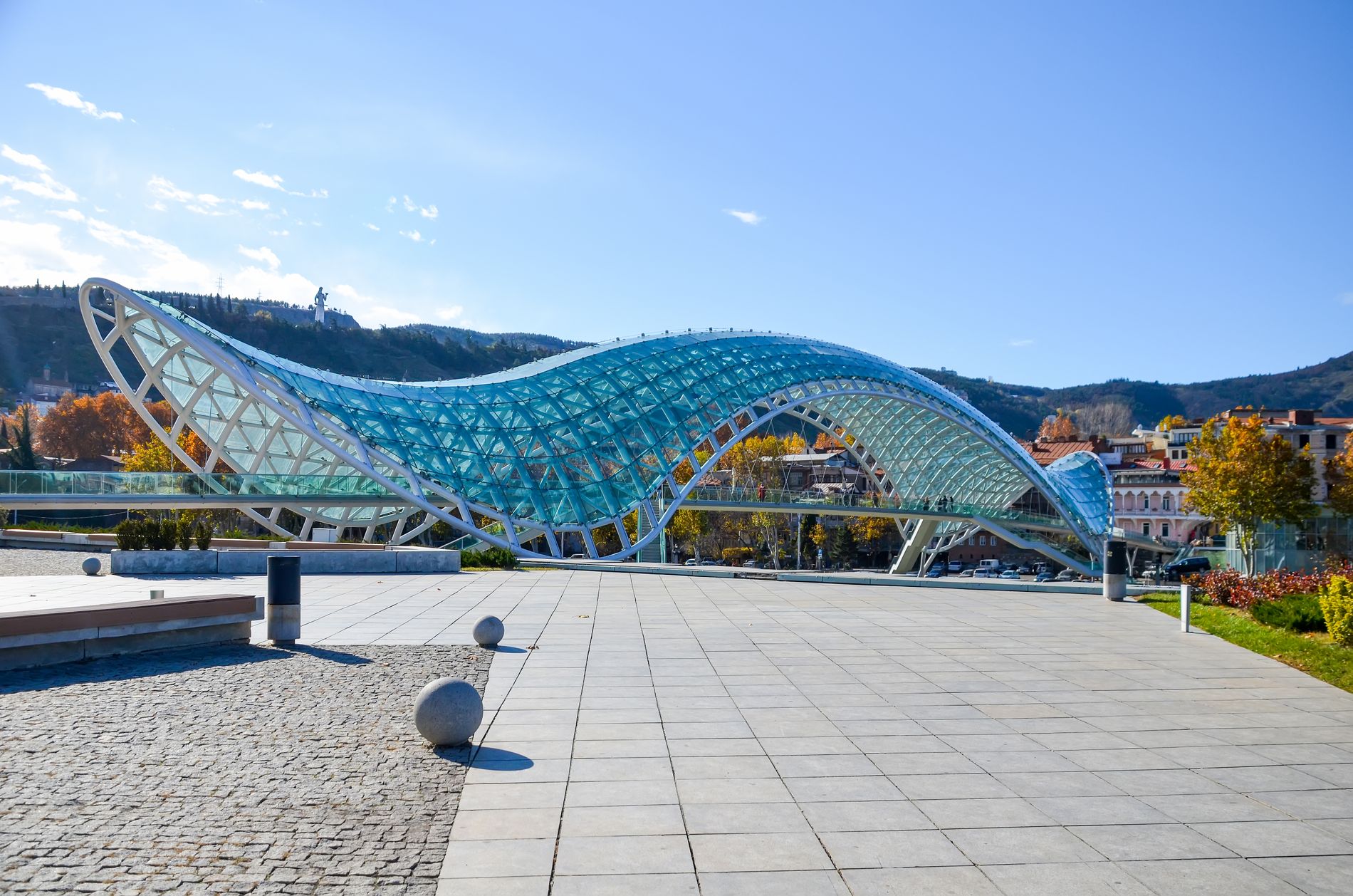 Complete view of the Bridge of Peace in Tbilisi — panoramic angle showing its full length, glass canopy and modern design