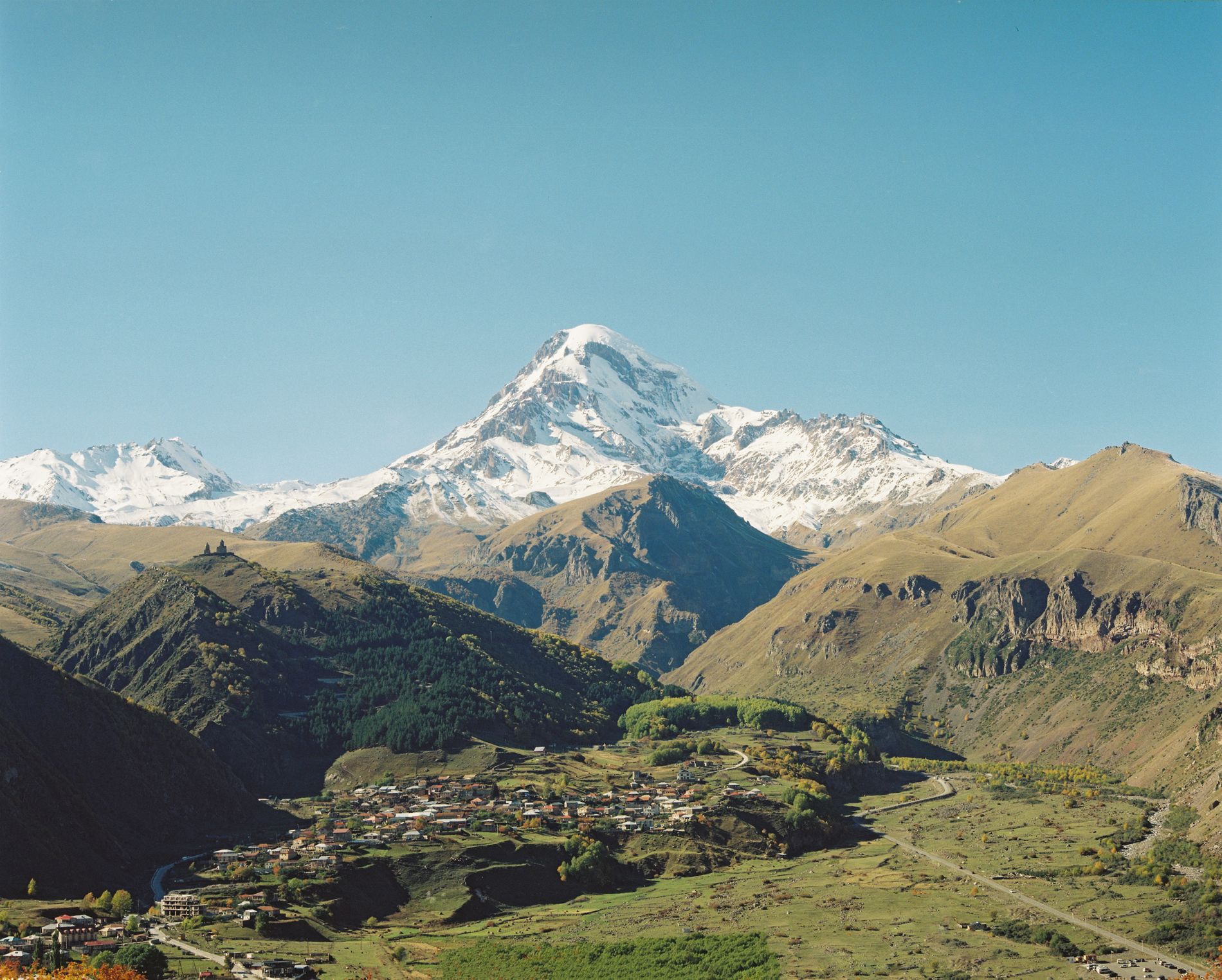 Snowy peaks of Kazbegi mountains towering above Stepantsminda village — dramatic mountain landscape in northern Georgia