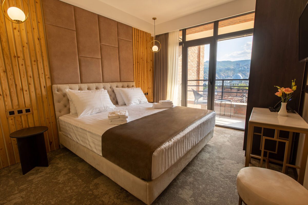 Deluxe room with double bed, soft natural light and balcony mountain view — boutique hotel stay in the heart of Georgia’s capital