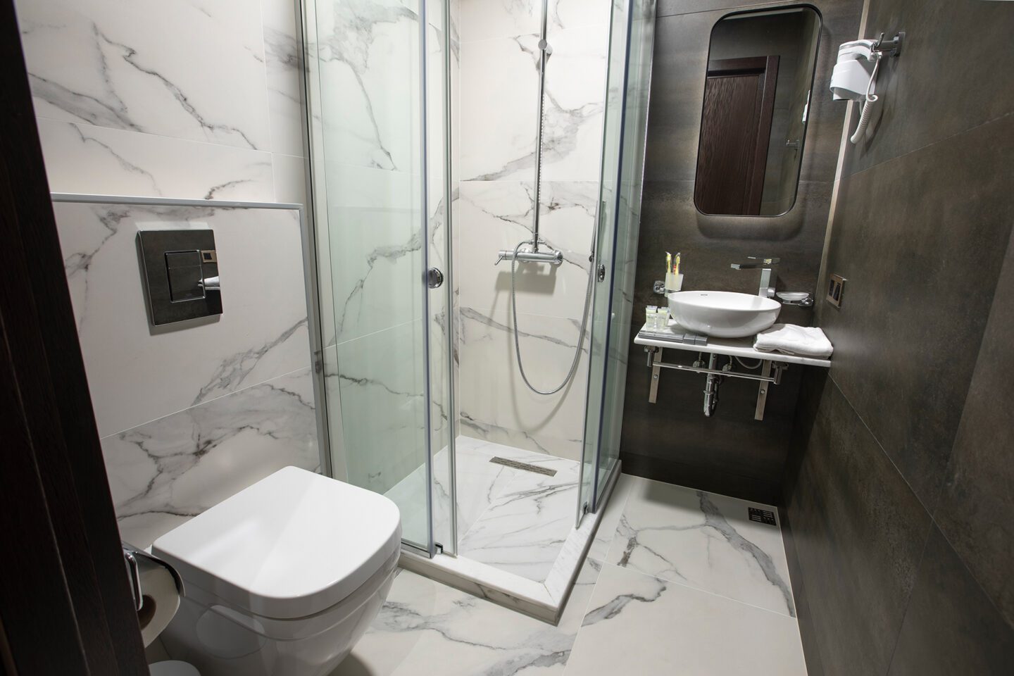 Sparkling clean hotel bathroom in Tbilisi — rain shower, modern toilet, marble walls and fresh towels at Bellevue Boutique Hotel