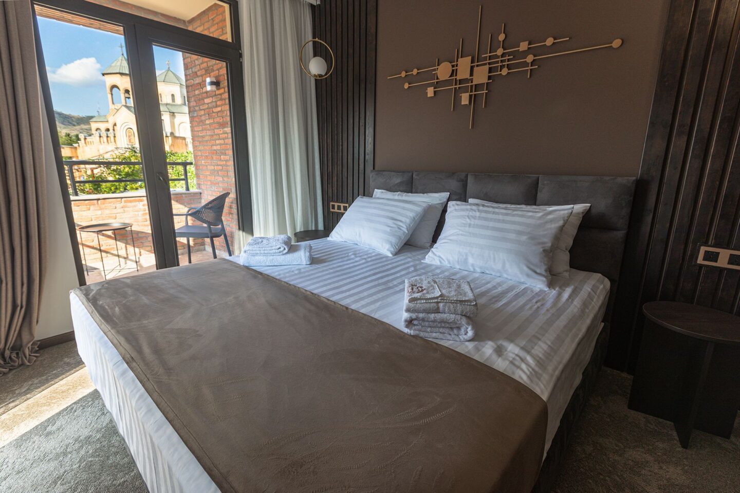 Elegant bed with soft headboard lights and full-height windows opening to a cathedral view — premier hotel room in Old Tbilisi
